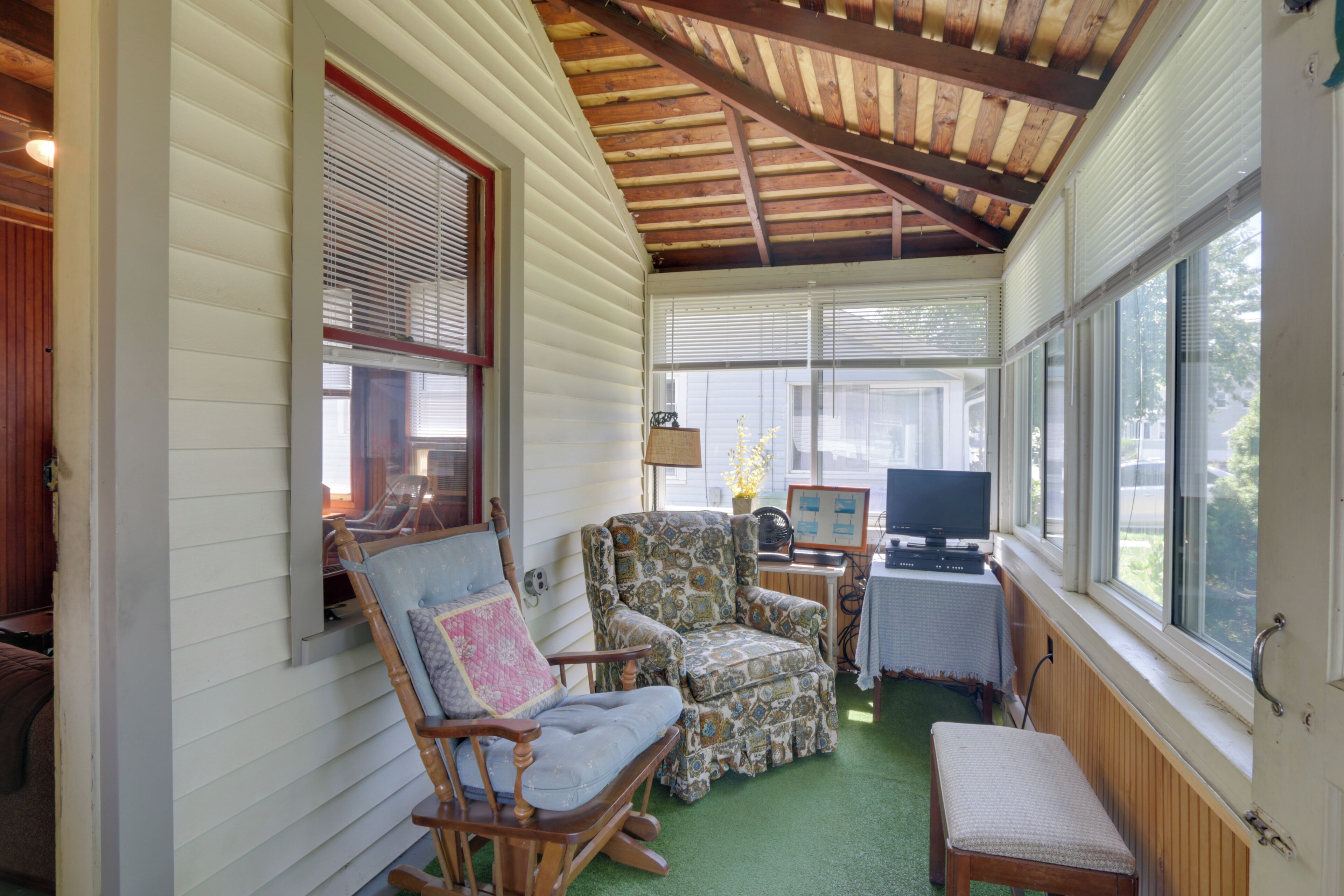 A cozy porch with a rocking chair, a cushioned chair, and a small table with a lamp and a television.