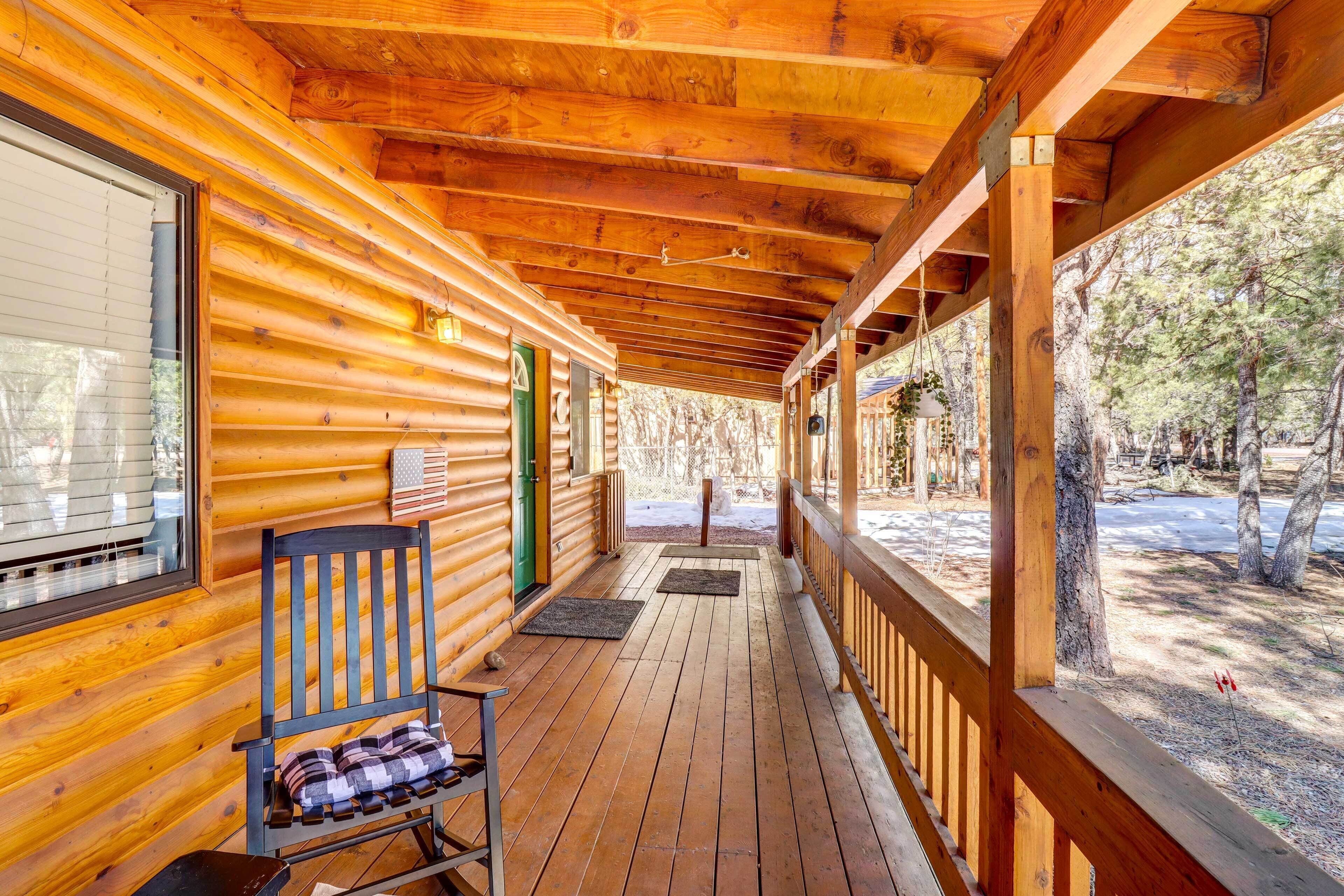 A wooden cabin with a covered porch, a rocking chair, and a view of the surrounding forest.
