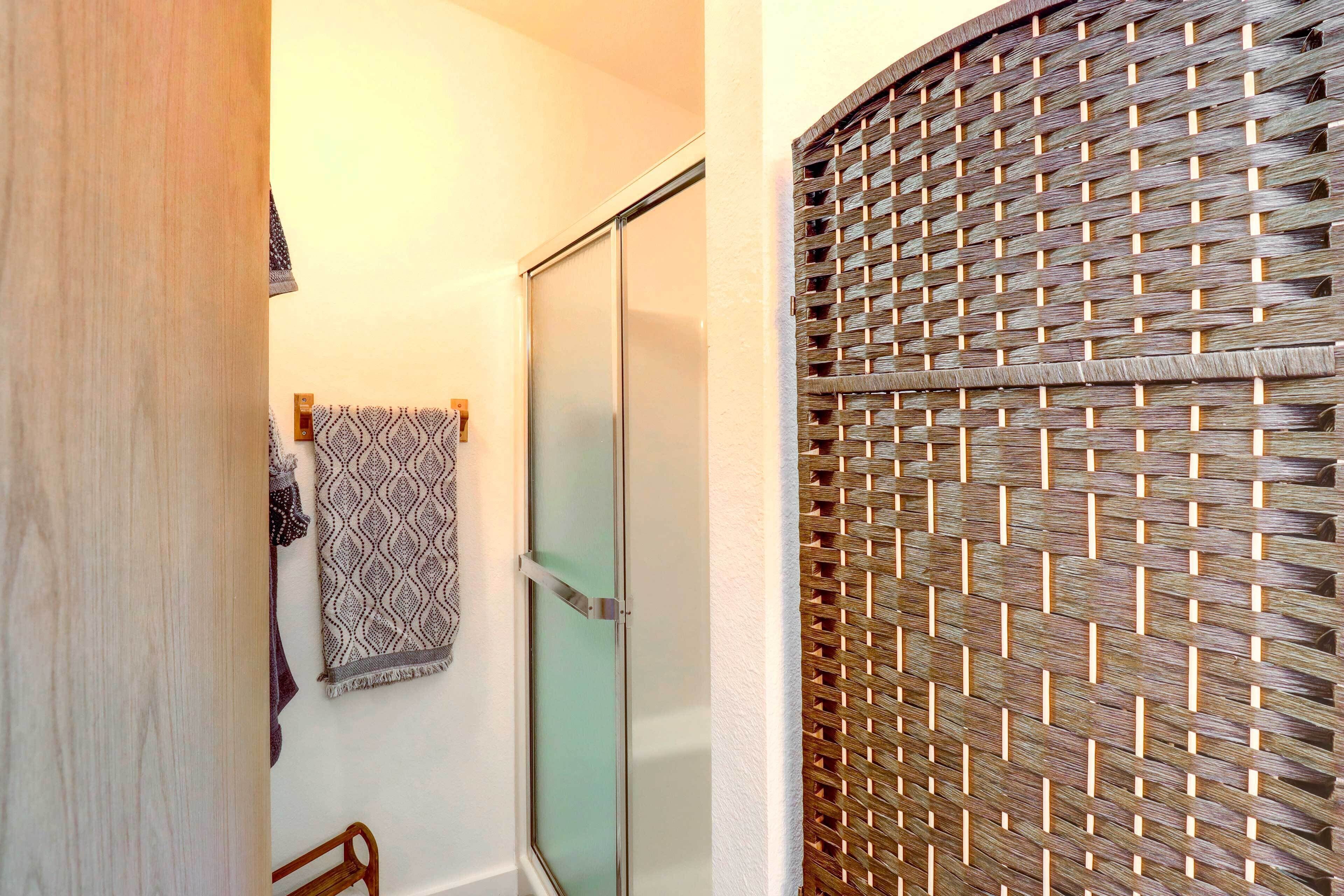 A bathroom with a glass shower door, a woven privacy screen, and patterned towels on the wall.