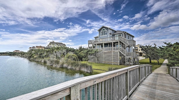 A waterfront property with a wooden deck, a large house with multiple levels, and a clear view of the water. - Avon Home on the Channel w/ Deck & Views! (Avon)