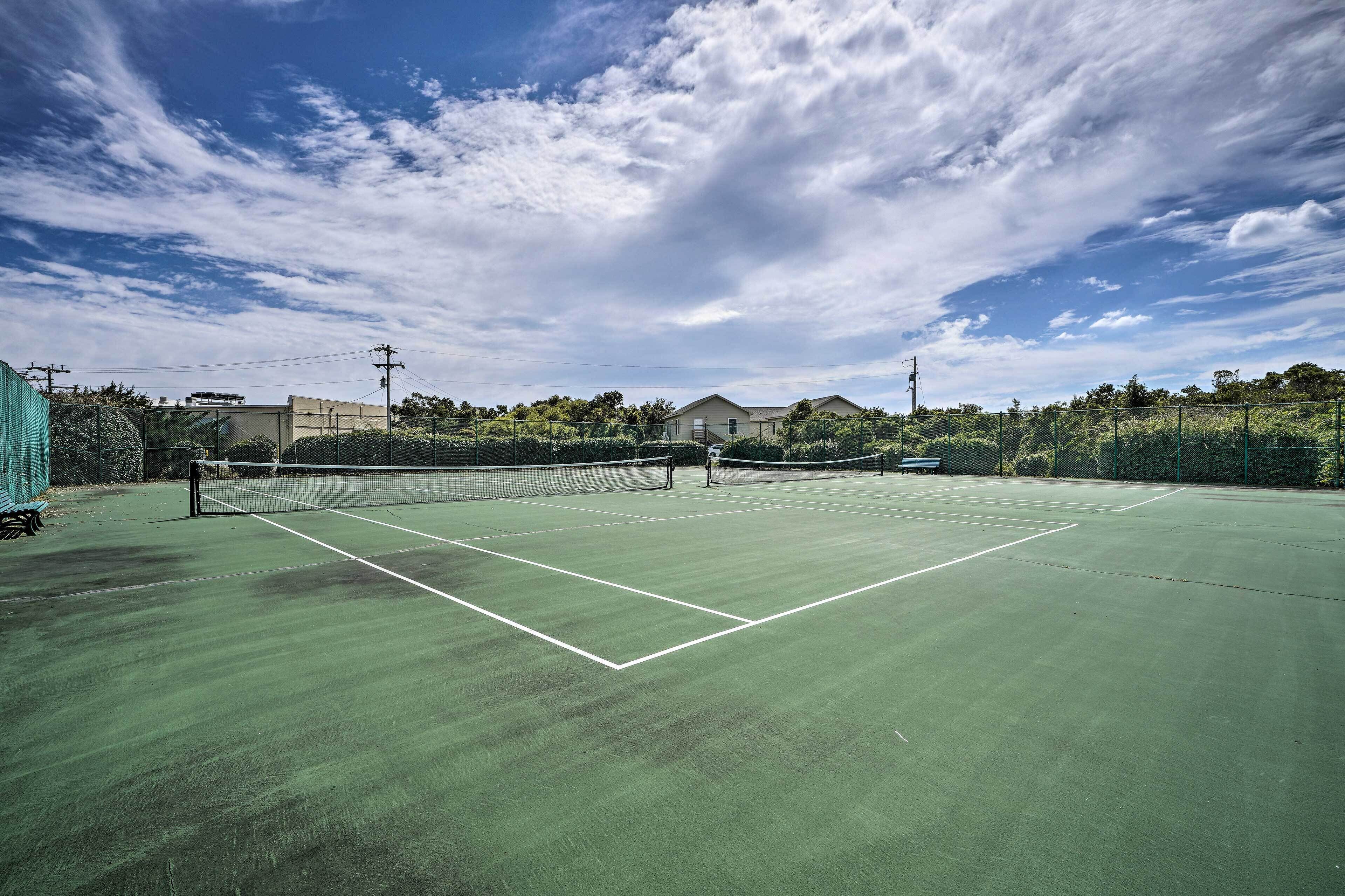A tennis court with a net, surrounded by greenery and buildings.