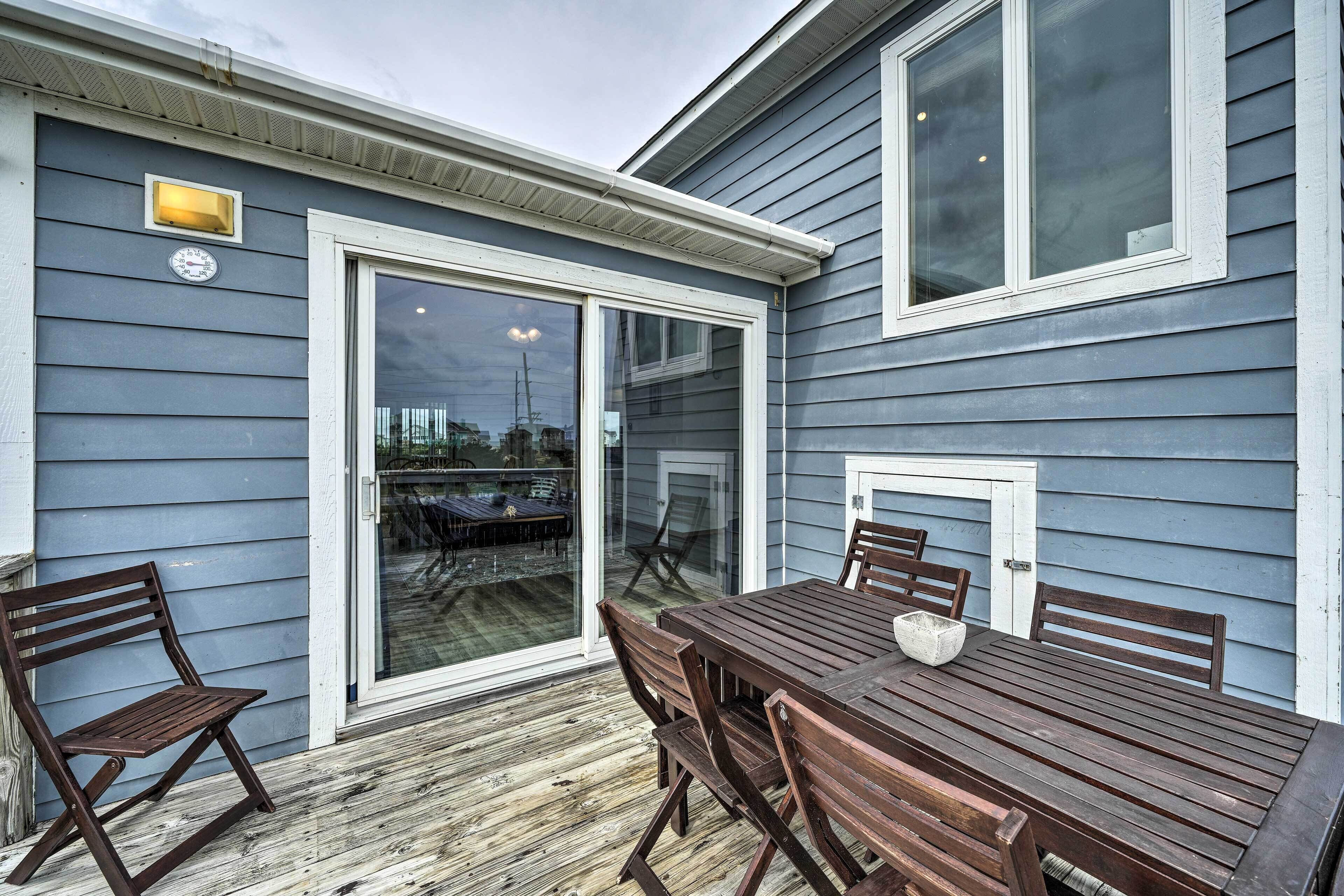 A wooden deck with a table and chairs, a sliding glass door, and a small outdoor seating area.