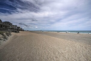 Una playa con un paseo marítimo de madera, una orilla arenosa y un cielo nublado.