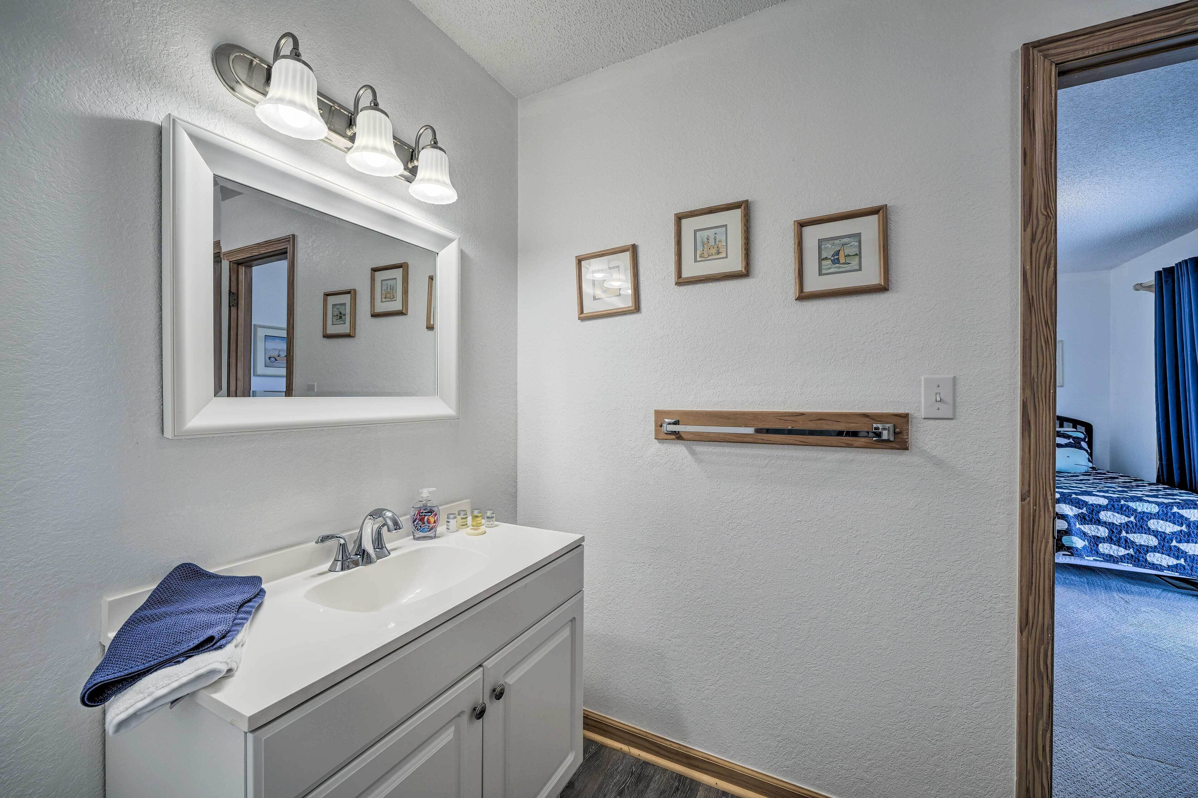 Une salle de bain avec un meuble-lavabo blanc, un miroir et trois tableaux encadrés accrochés au mur.