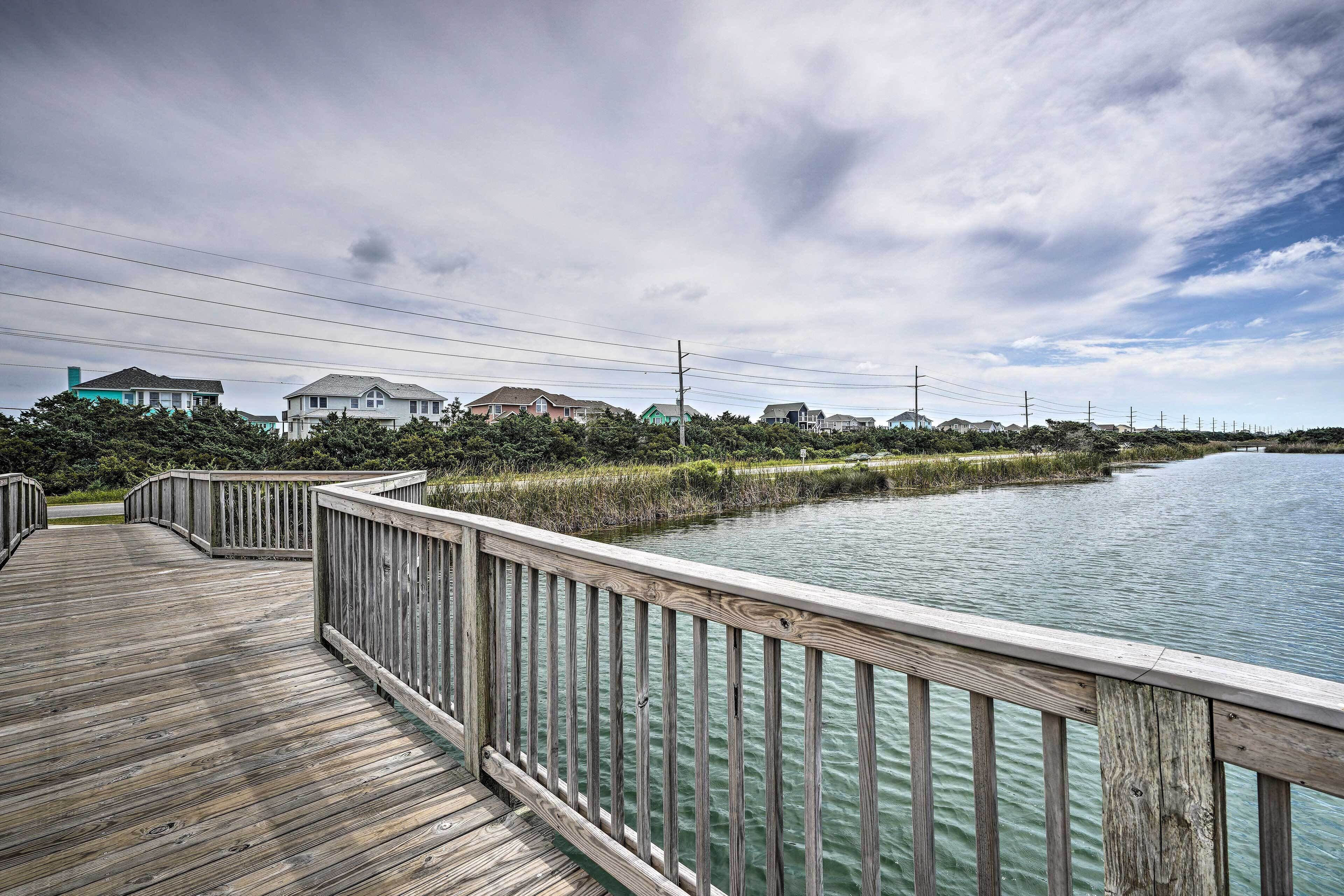 A wooden boardwalk leading to a body of water with houses in the background.