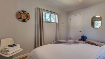 A bedroom with a bed, a chair, a window with curtains, a door, and a wall-mounted mirror.