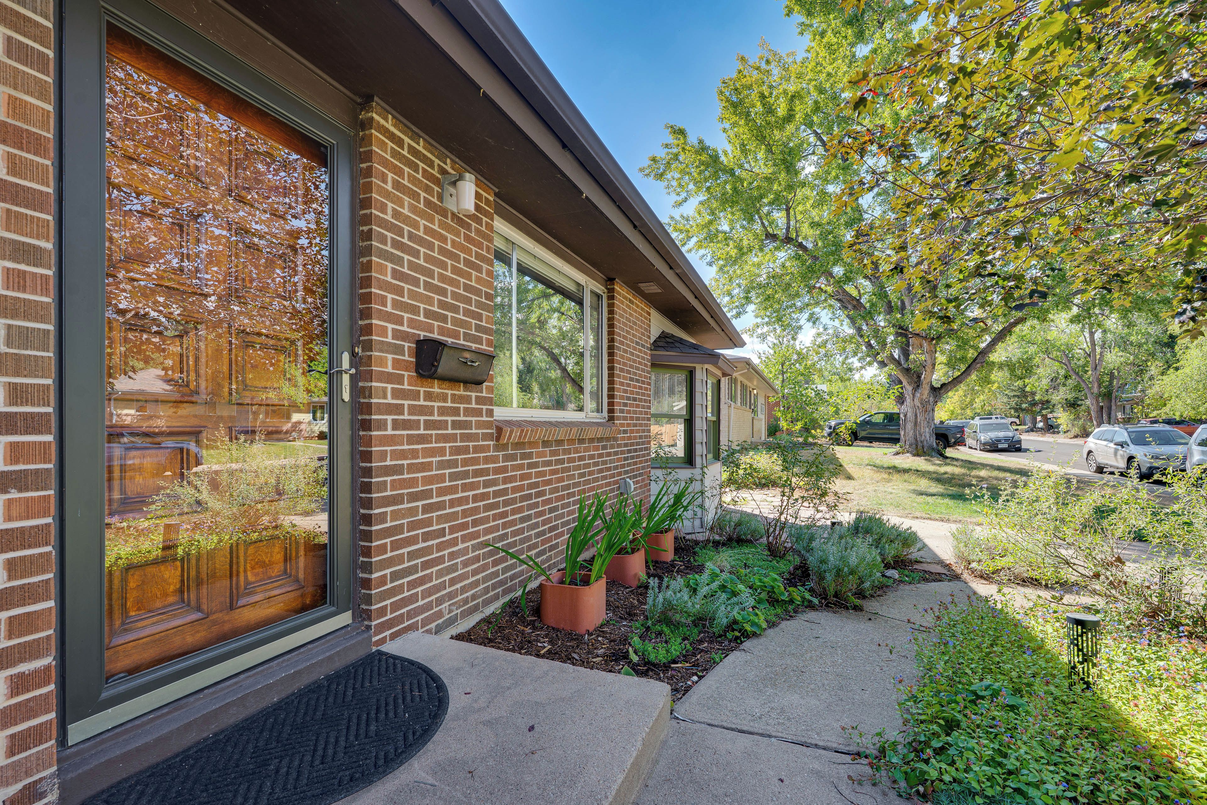 A residential building with a brick facade, large windows, and a well-maintained garden with potted plants.