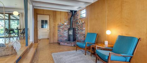 A cozy room with a fireplace, wooden walls, a ceiling fan, and a seating area with chairs and a table.