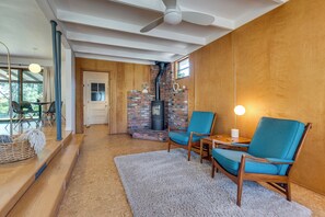 Une pièce chaleureuse avec une cheminée, des murs en bois, un ventilateur de plafond et un coin salon avec des chaises et une table.