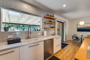 A modern kitchen with white cabinets, a stainless steel dishwasher, and a window with a view of greenery.