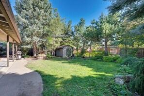 A residential backyard with a covered patio, a small shed, and a variety of trees and shrubs.