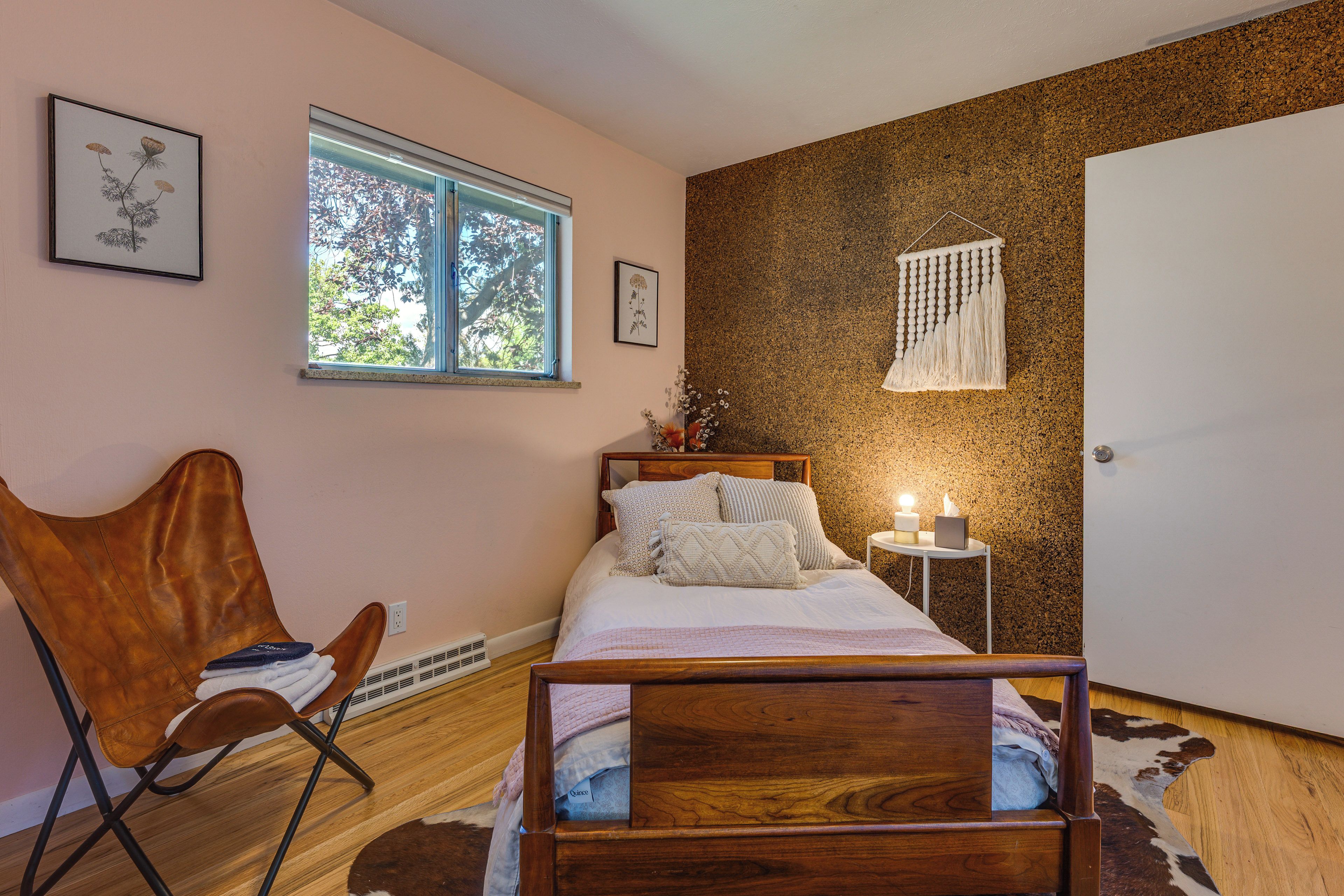 Un dormitorio con cama de madera, una silla, un ventanal y un adorno de macramé en la pared.