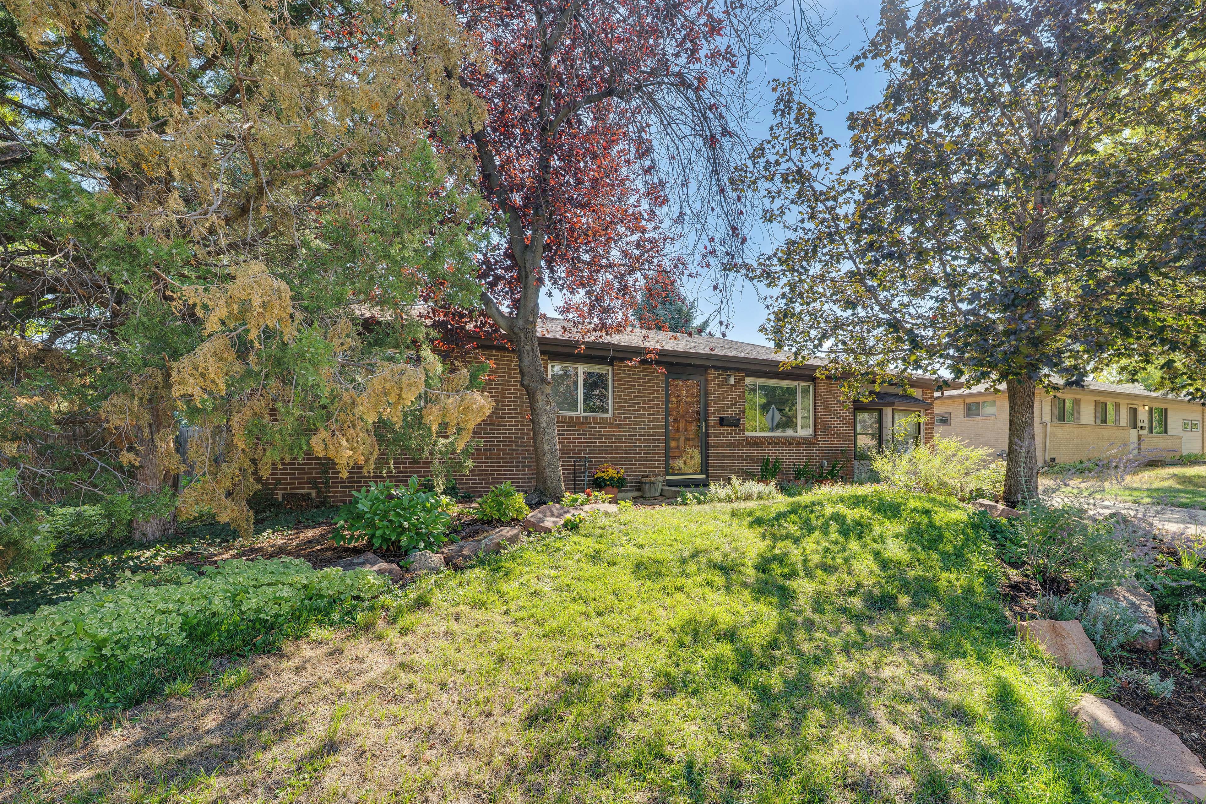 A single-story brick house with a front yard, surrounded by trees and shrubs.