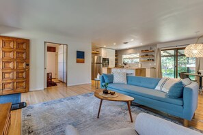 A modern living room with a blue sofa, a wooden coffee table, and a kitchen area with a refrigerator and microwave. - < 3 Mi to Pearl St: Home w/ Large Yard in Boulder (Boulder)
