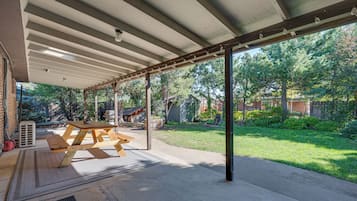 A covered patio area with a picnic table and a large window overlooking a backyard.