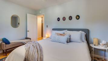 A bedroom with a bed, bedside table, lamp, and a mirror on the wall.