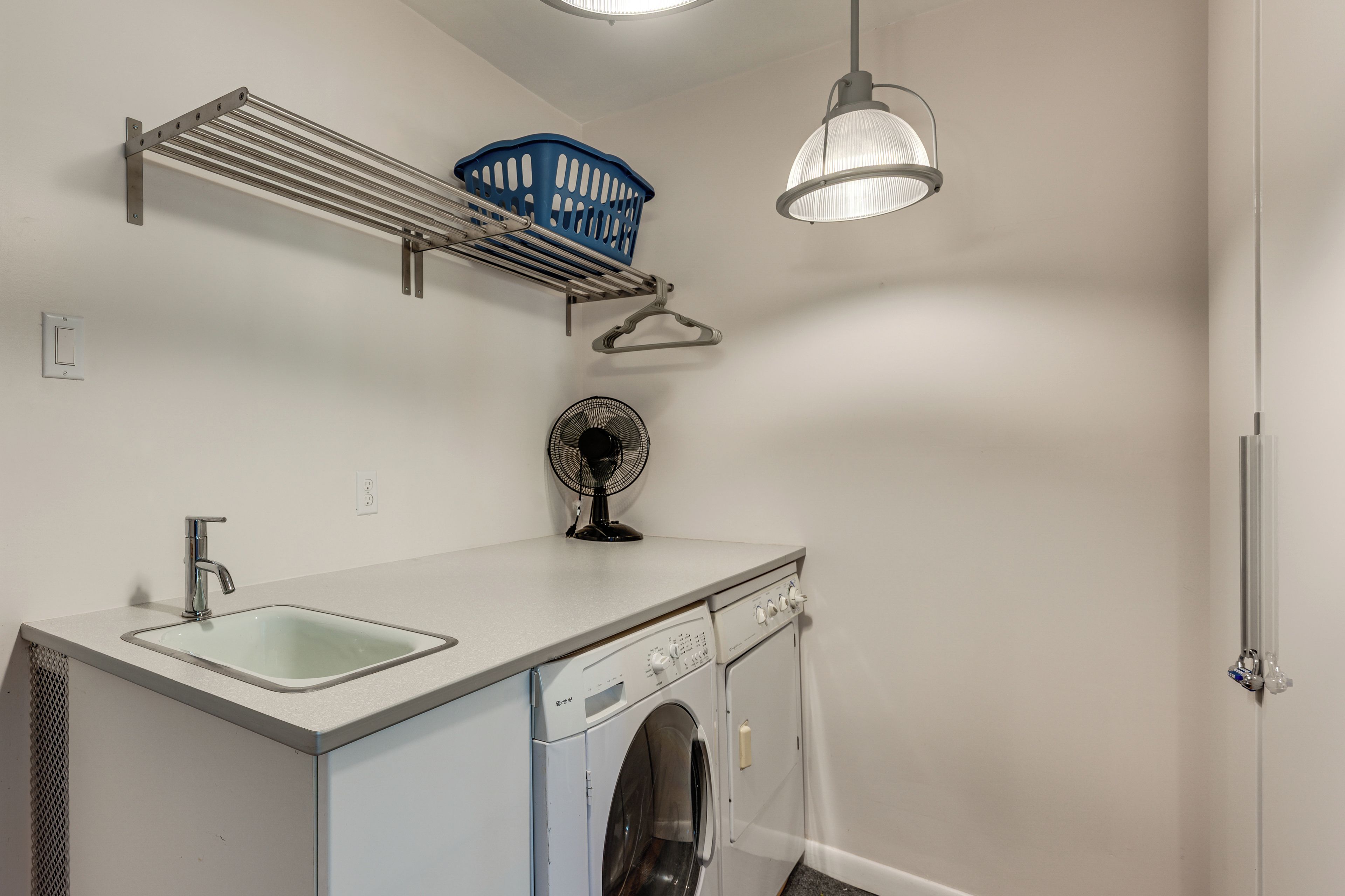 A laundry room with a washing machine, a sink, a fan, and a ceiling-mounted light fixture.