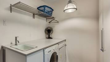 A laundry room with a washing machine, a sink, a fan, and a ceiling-mounted light fixture.
