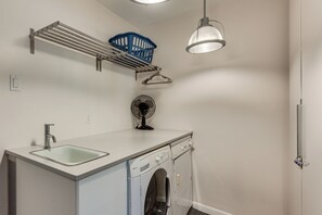 A laundry room with a washing machine, a sink, a fan, and a ceiling-mounted light fixture.