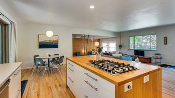 A modern kitchen with a central island, dining area with chairs, and a living room with a sofa and TV.