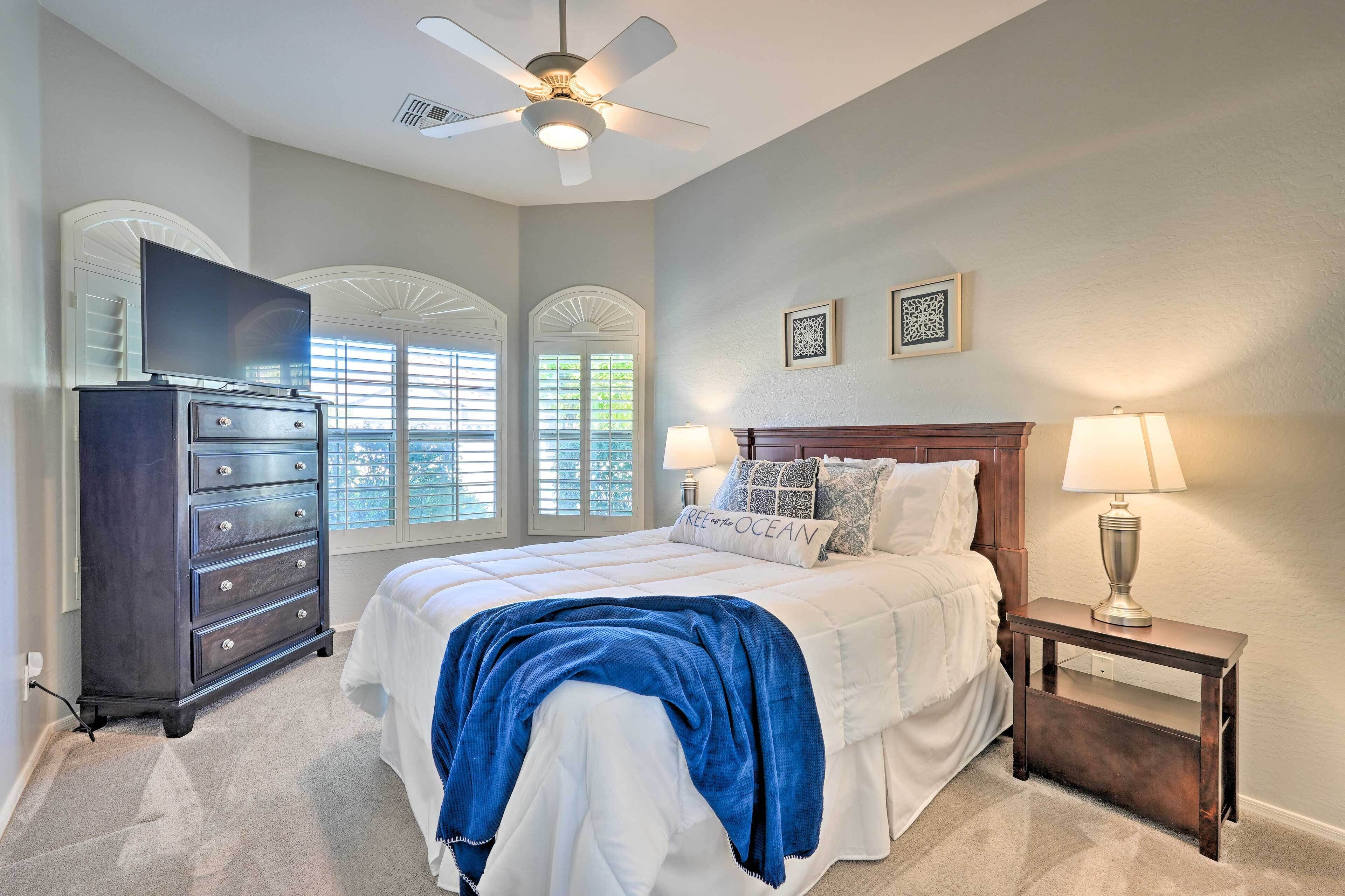 A bedroom with a bed, dresser, TV, and a nightstand with a lamp.
