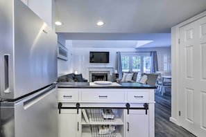 A compact kitchen with a built-in refrigerator, a flat-screen TV above the counter, and a dining area with a table and chairs.