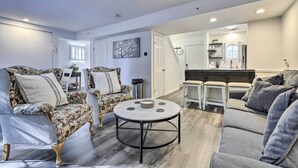 A modern living room with a round coffee table, floral armchairs, and a grey sofa. A kitchen area is visible in the background.