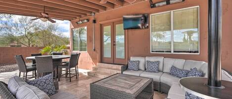An outdoor patio area with a ceiling fan, wicker furniture, a TV mounted on the wall, and a view of the surrounding landscape.