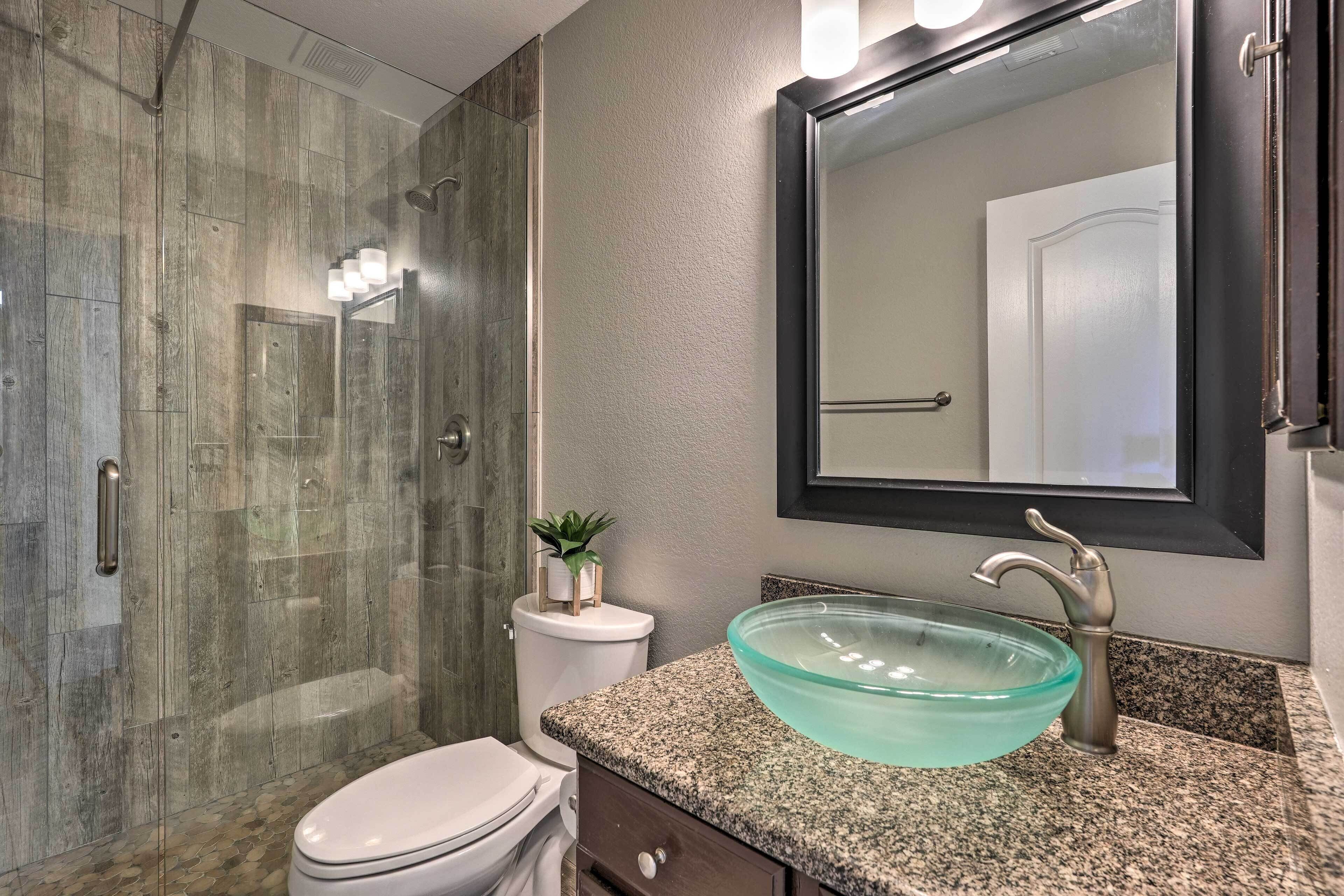 Une salle de bain moderne dotée d’une douche à parois de verre, de toilettes, d’un lavabo avec un receveur en verre et d’un grand miroir.