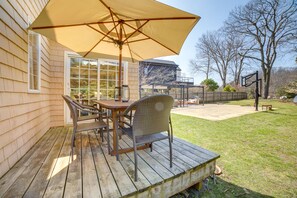 A wooden deck with a table and chairs, a large umbrella, and a view of a house and trees. - Lovely Kalamazoo River Home w/ Dock & Hot Tub (Saugatuck)
