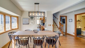 Un comedor con una mesa y sillas de madera, una lámpara colgante y vistas a la cocina y la escalera.