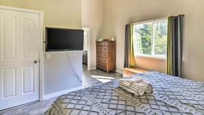 Een slaapkamer met een bed, een aan de muur bevestigde televisie, een dressoir en een raam met gordijnen.