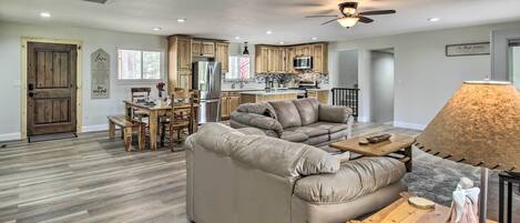 A spacious living room with a large beige sectional sofa, a wooden coffee table, and a dining area with a wooden table and chairs.