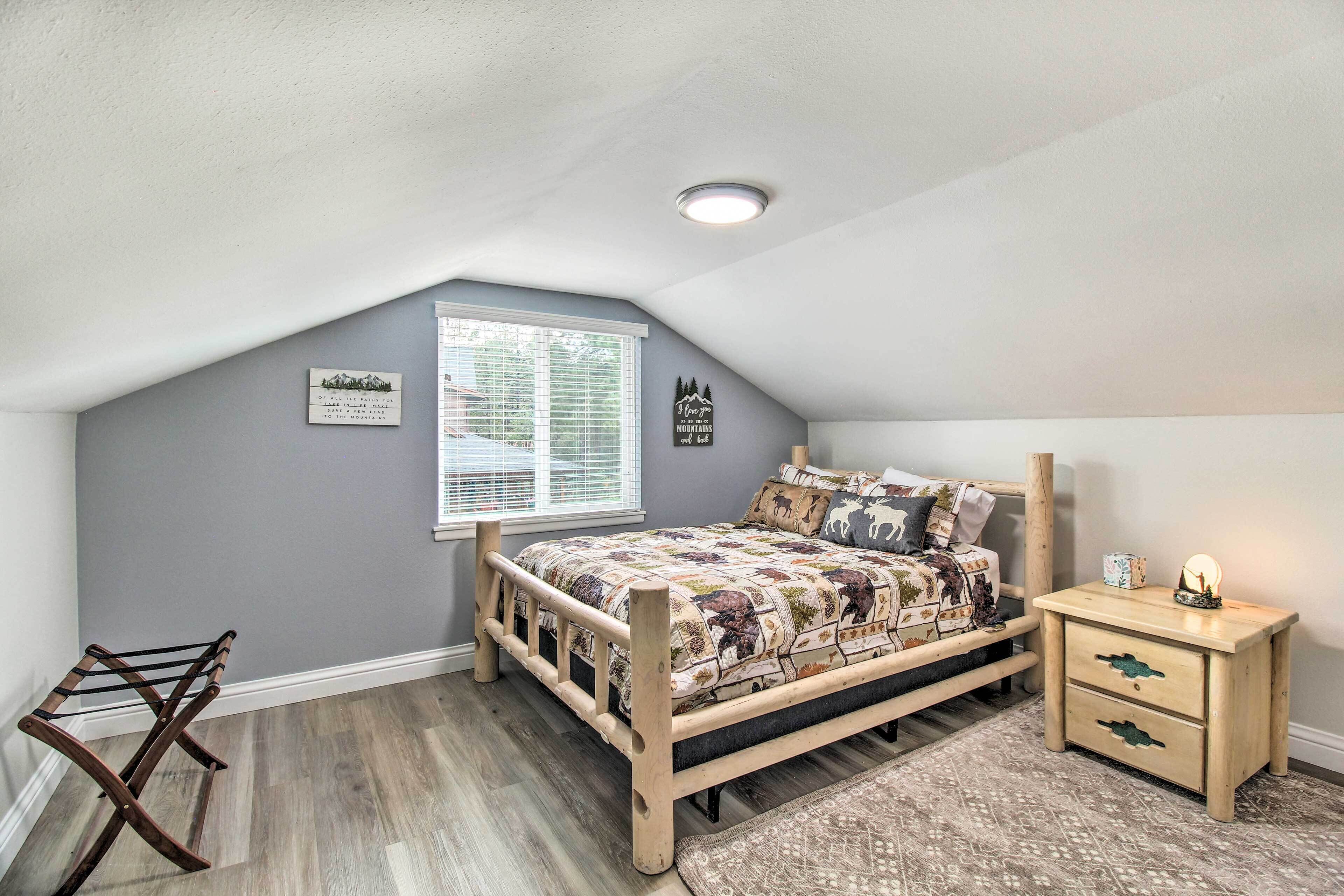 A bedroom with a sloped ceiling, a wooden bed, a nightstand, a window with blinds, and a wall-mounted towel rack.