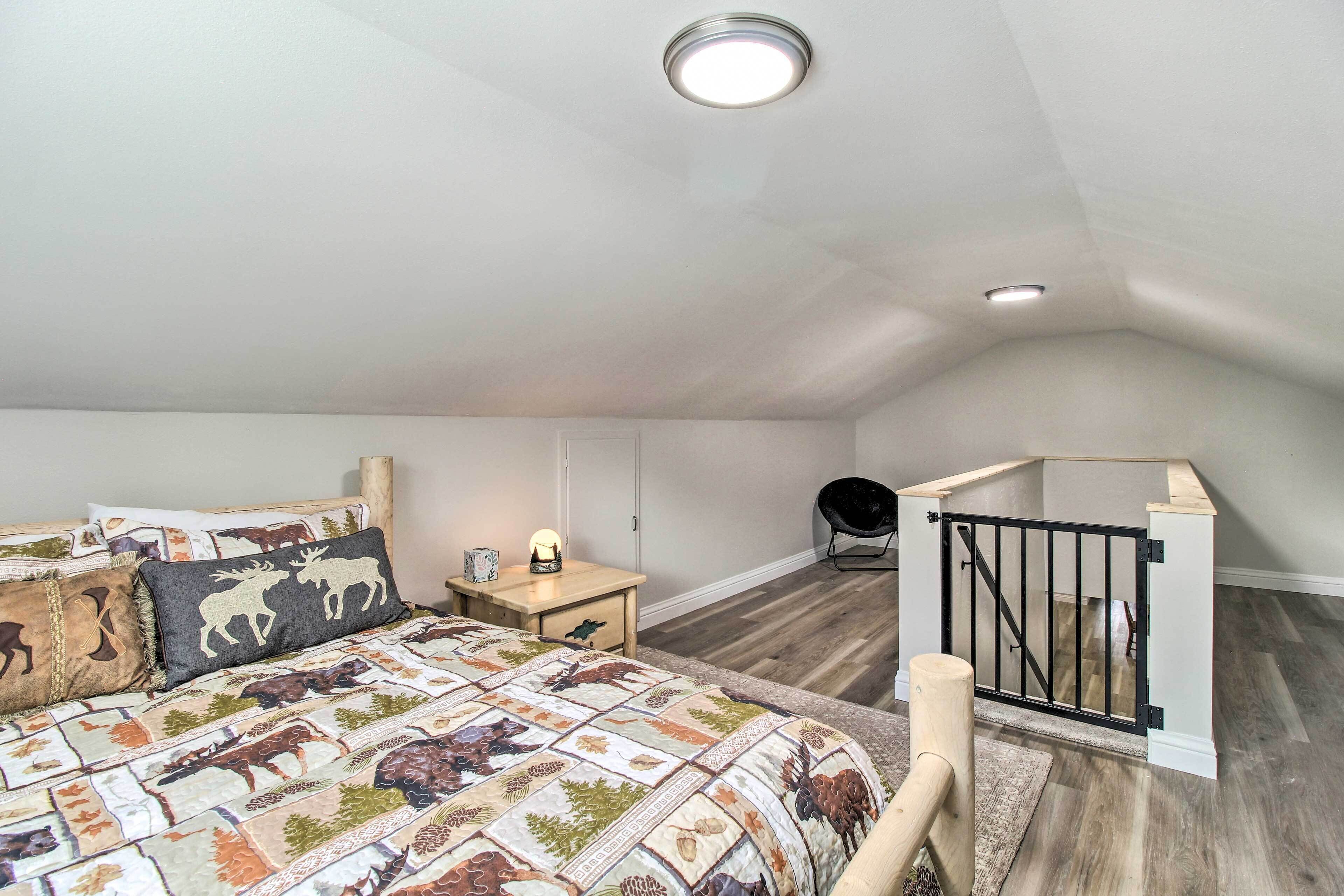 A bedroom with a bed, a nightstand, a lamp, a chair, and a staircase.