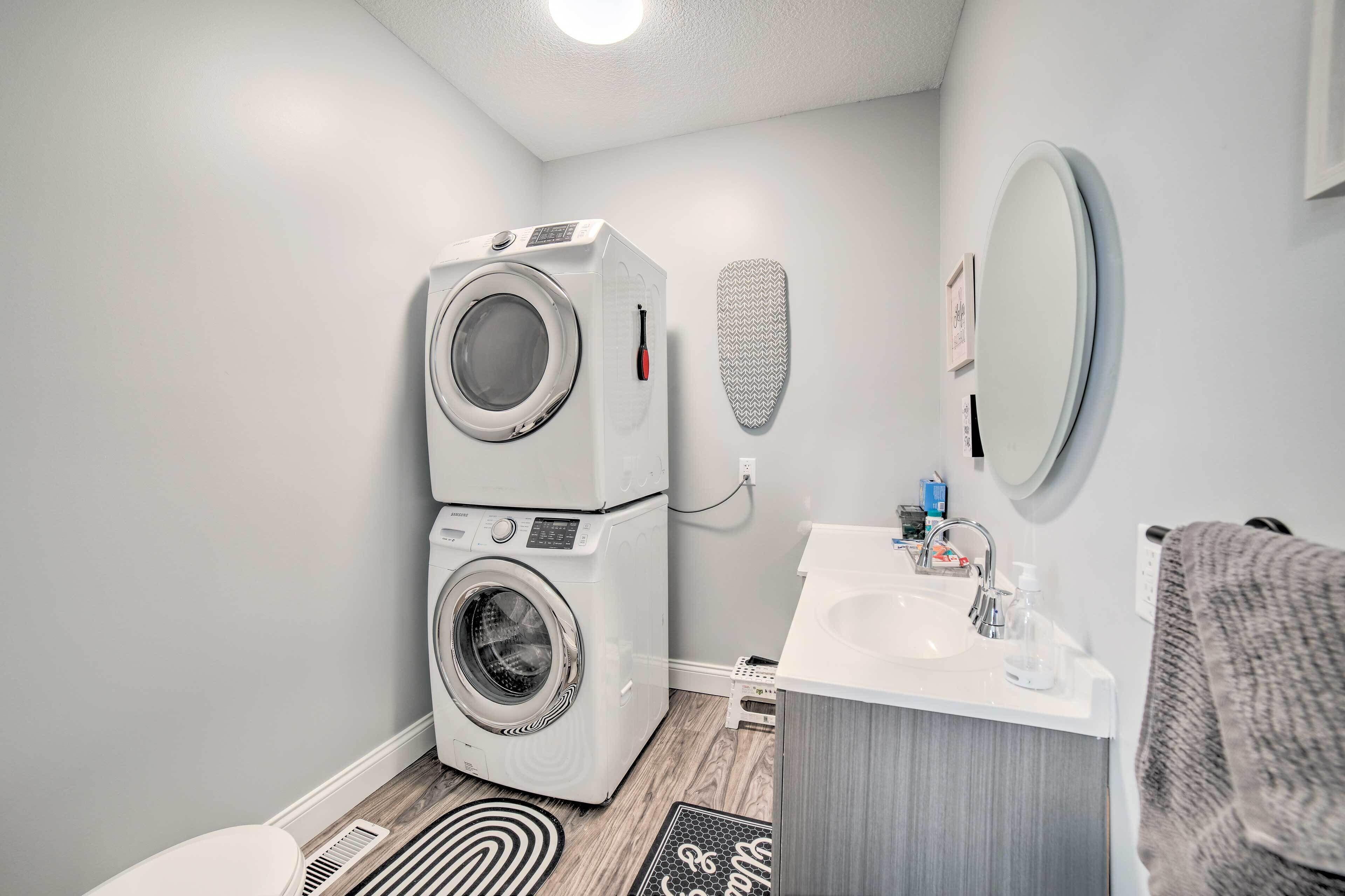 A compact laundry room with a front-loading washer and dryer, a small sink with a mirror, and a towel rack.