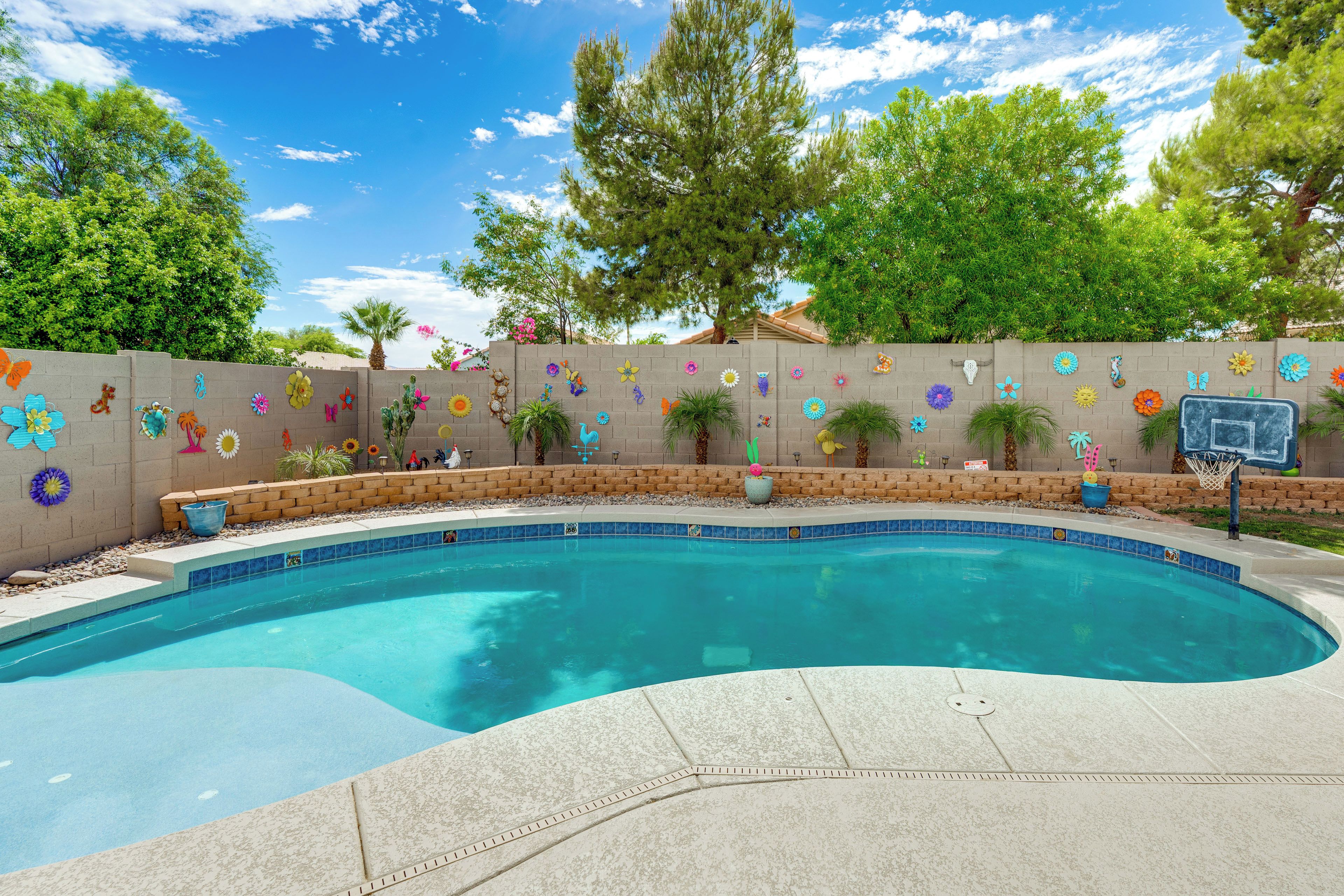 A swimming pool with a tiled edge, surrounded by a brick wall with colorful flower decorations.