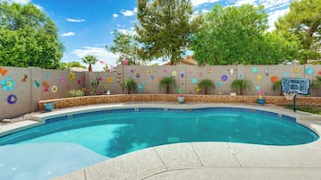 A swimming pool with a tiled edge, surrounded by a brick wall with colorful flower decorations.