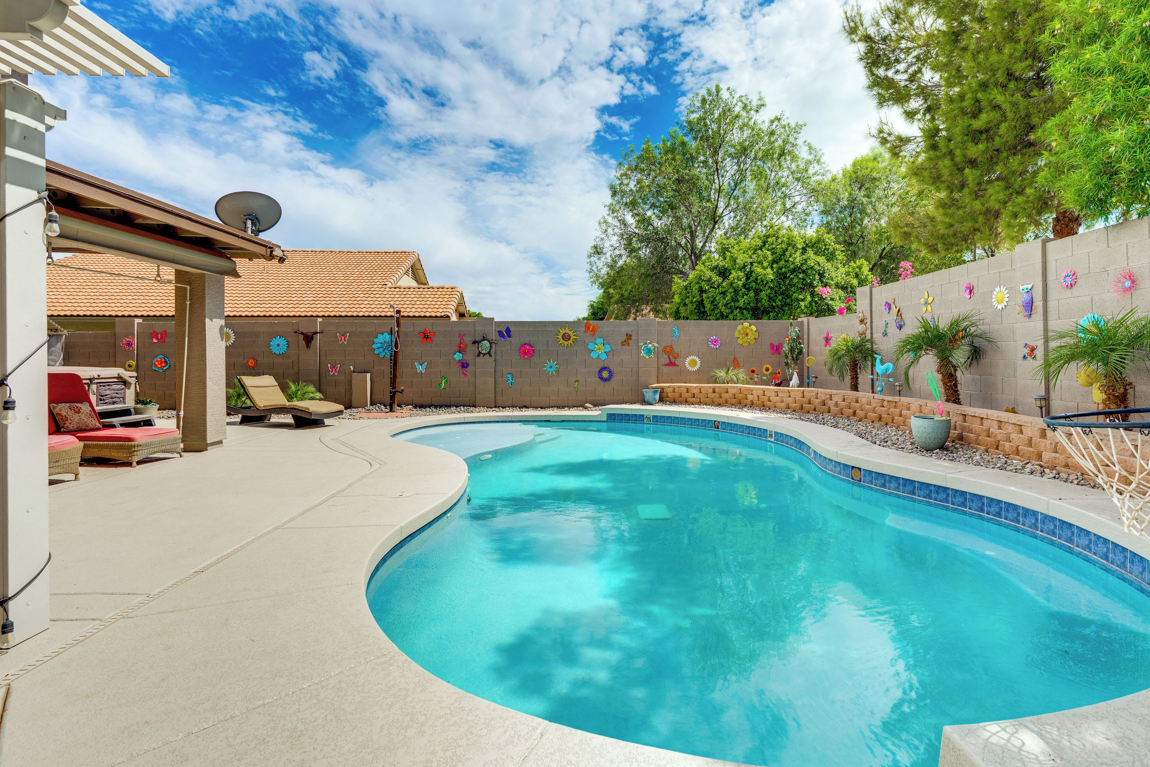 A swimming pool with a curved edge, a patio area with lounge chairs, and a decorative wall with colorful patterns.