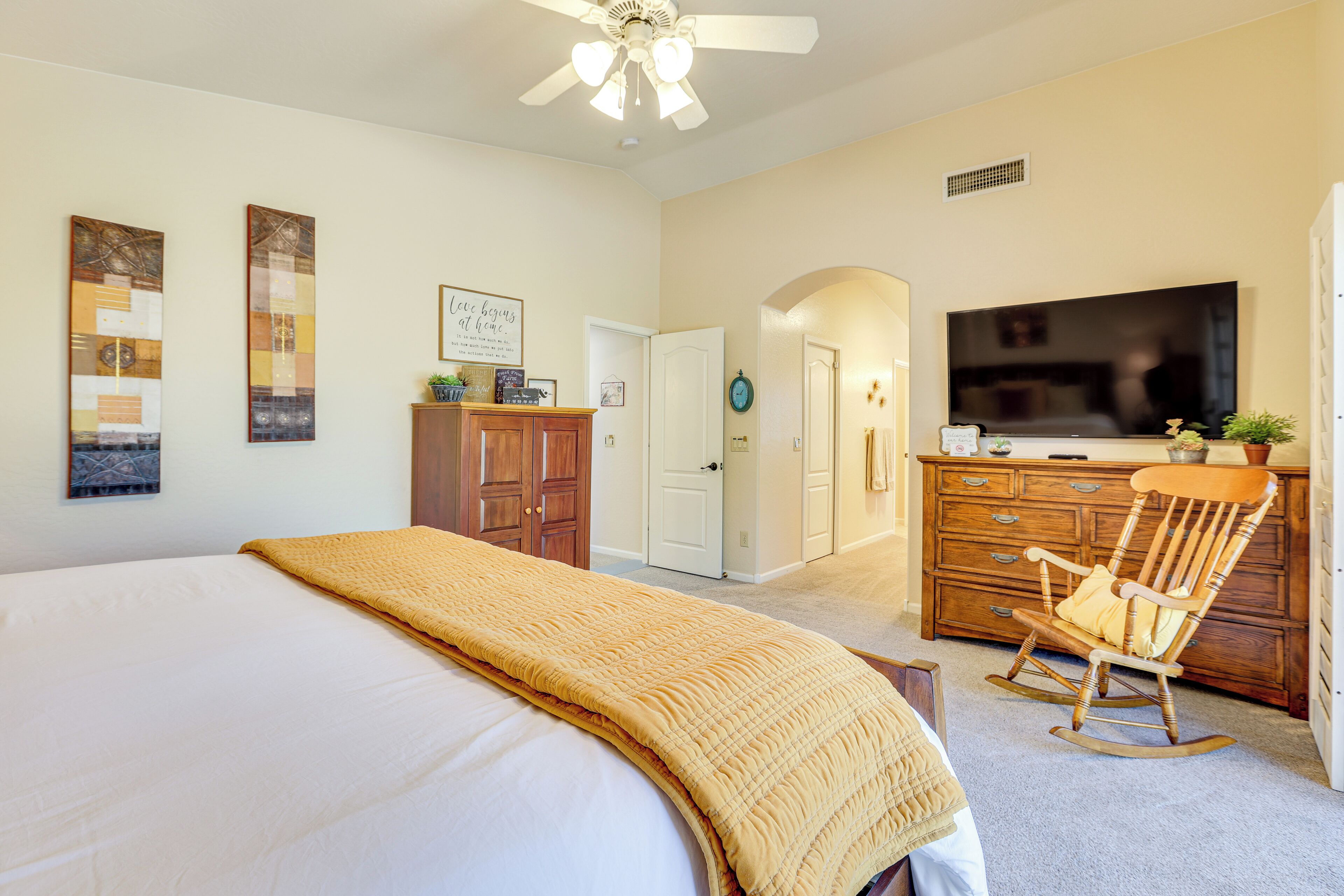 A bedroom with a large bed, a wooden dresser, a television, and a rocking chair.