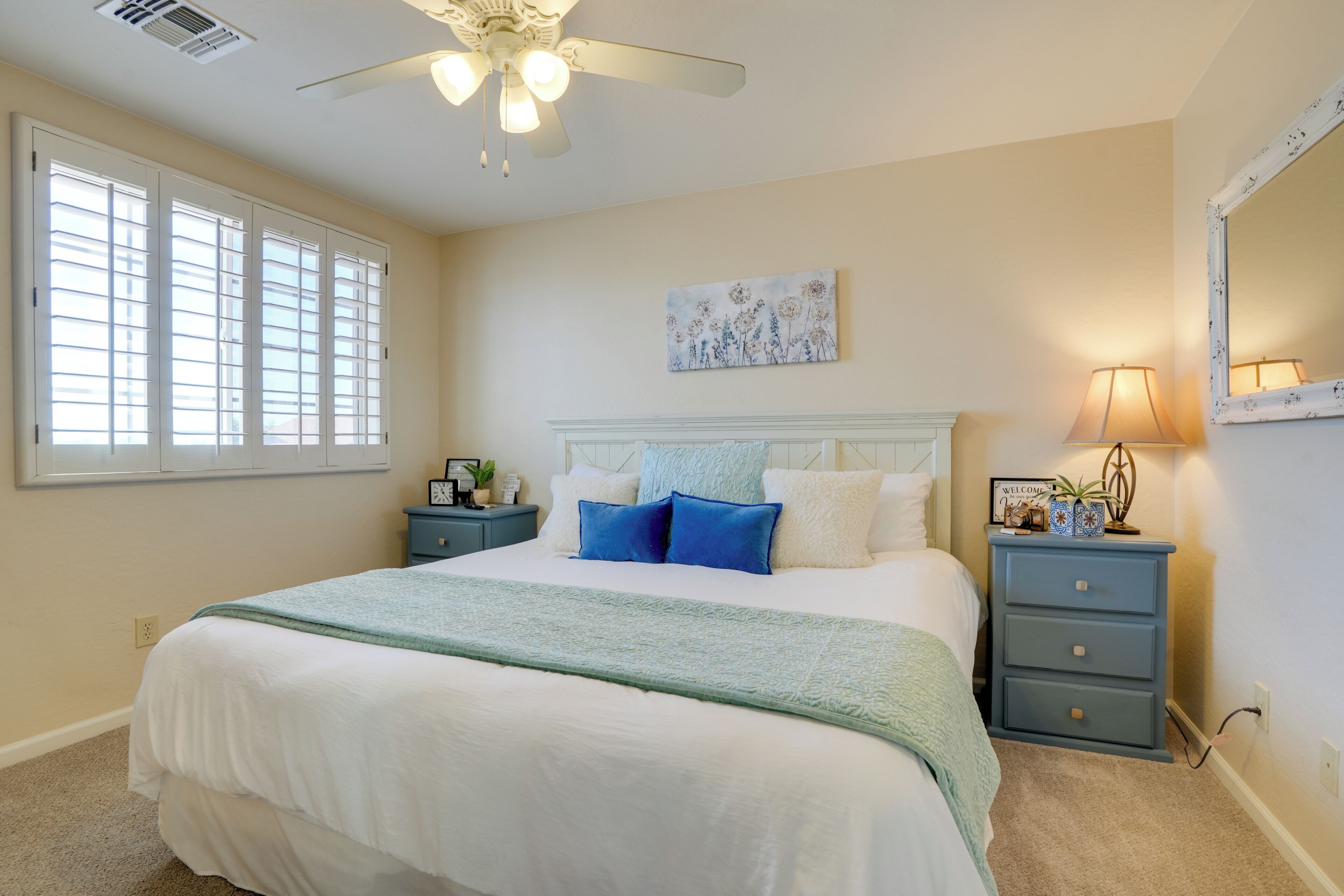 A bedroom with a bed, a nightstand, a lamp, a ceiling fan, and a window with blinds.