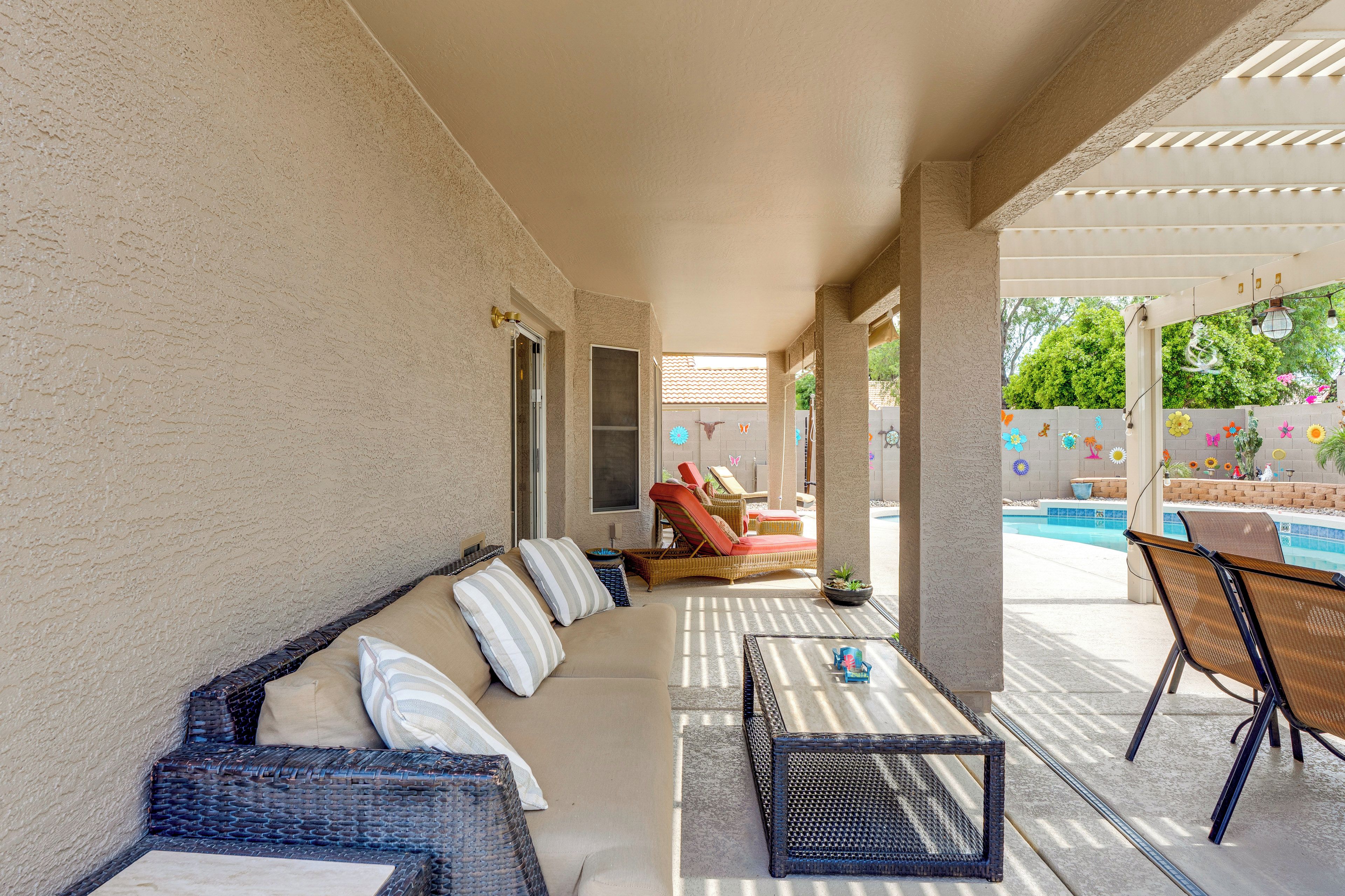 Un patio cubierto con sofá, sillas, una mesa y una piscina al fondo.