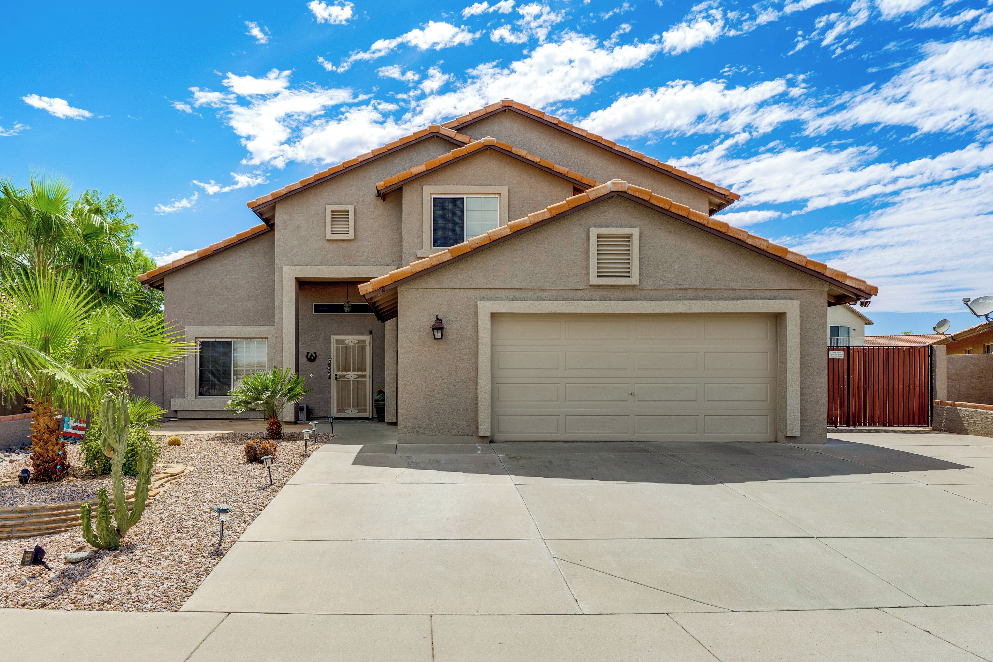 A two-story house with a garage, a driveway, and a small garden with cacti and palm trees.
