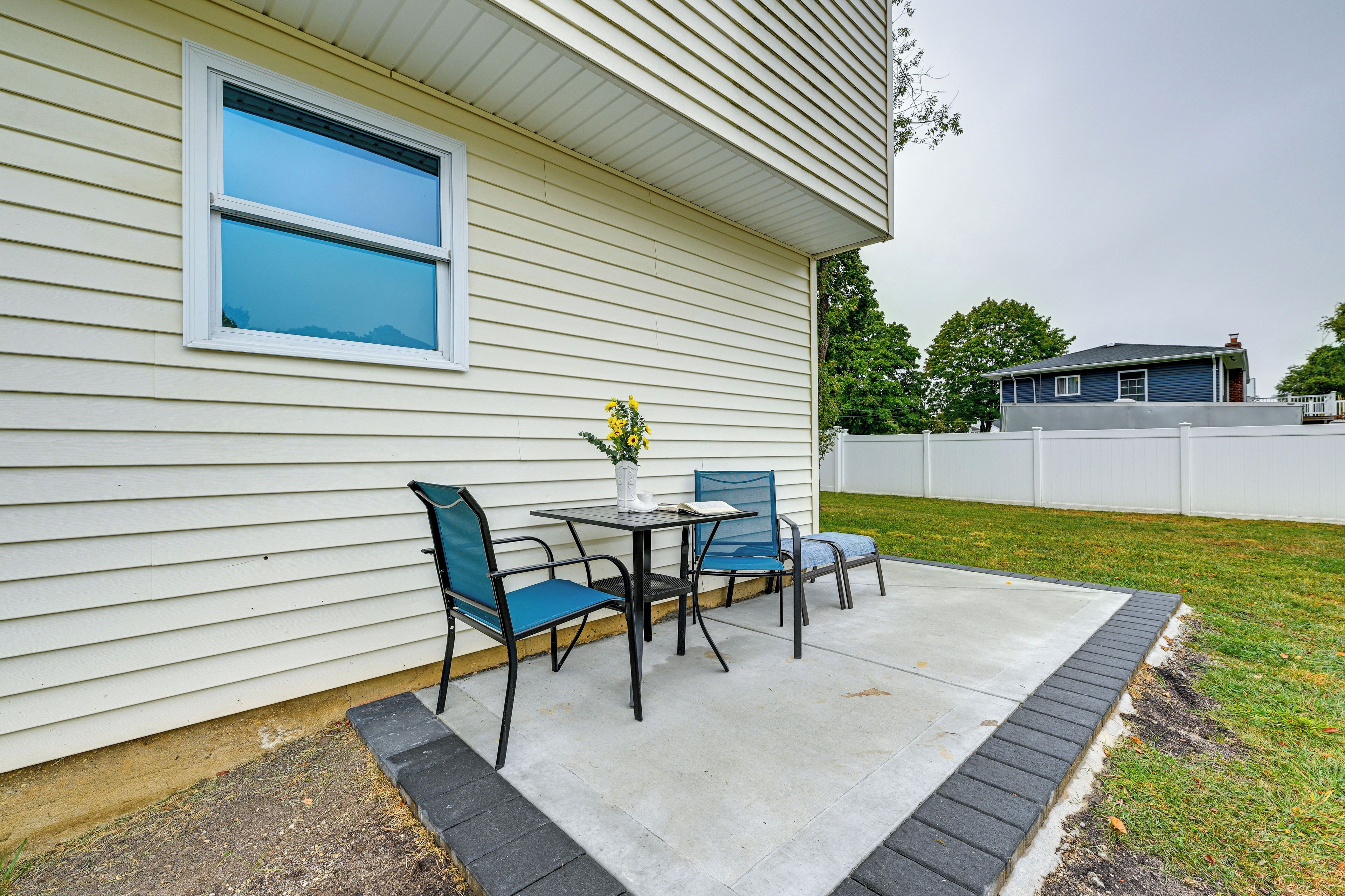 A patio with a table and chairs, a window, and a white fence.