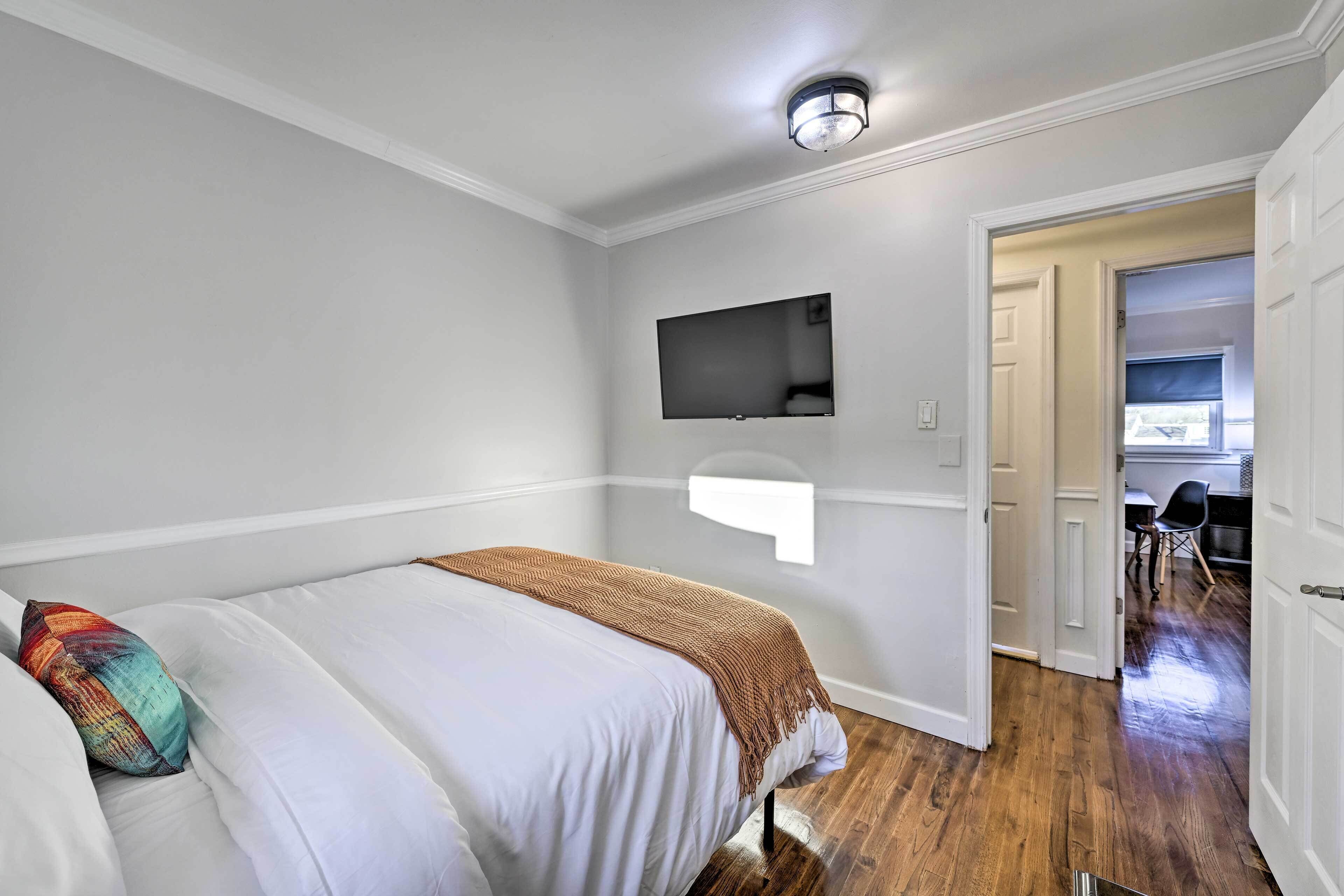 Ein Schlafzimmer mit einem Bett, einem an der Wand befestigten Fernseher und einer Tür zu einem Essbereich.