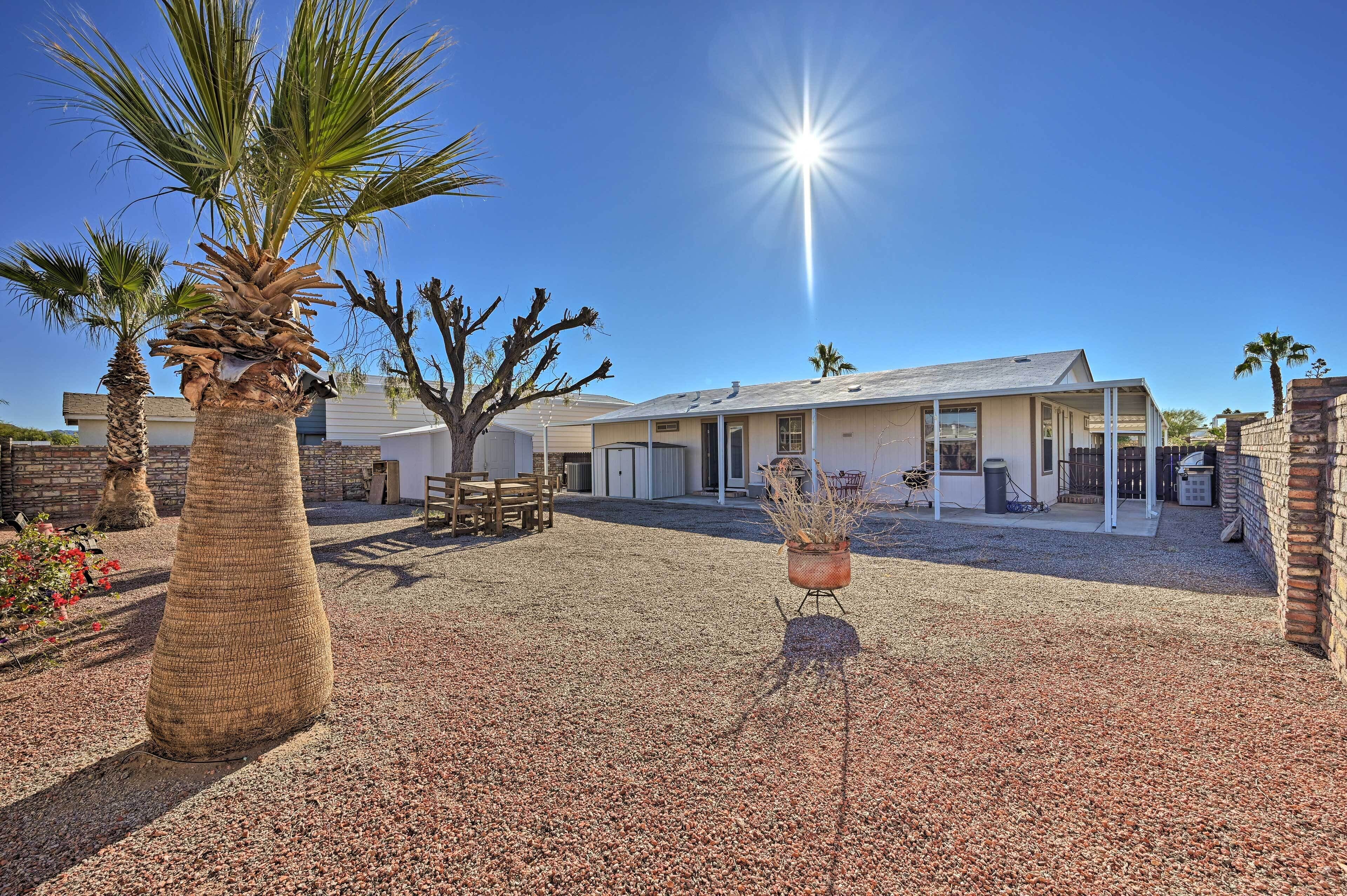 A house with a gravel driveway, palm trees, and a patio area with outdoor furniture.
