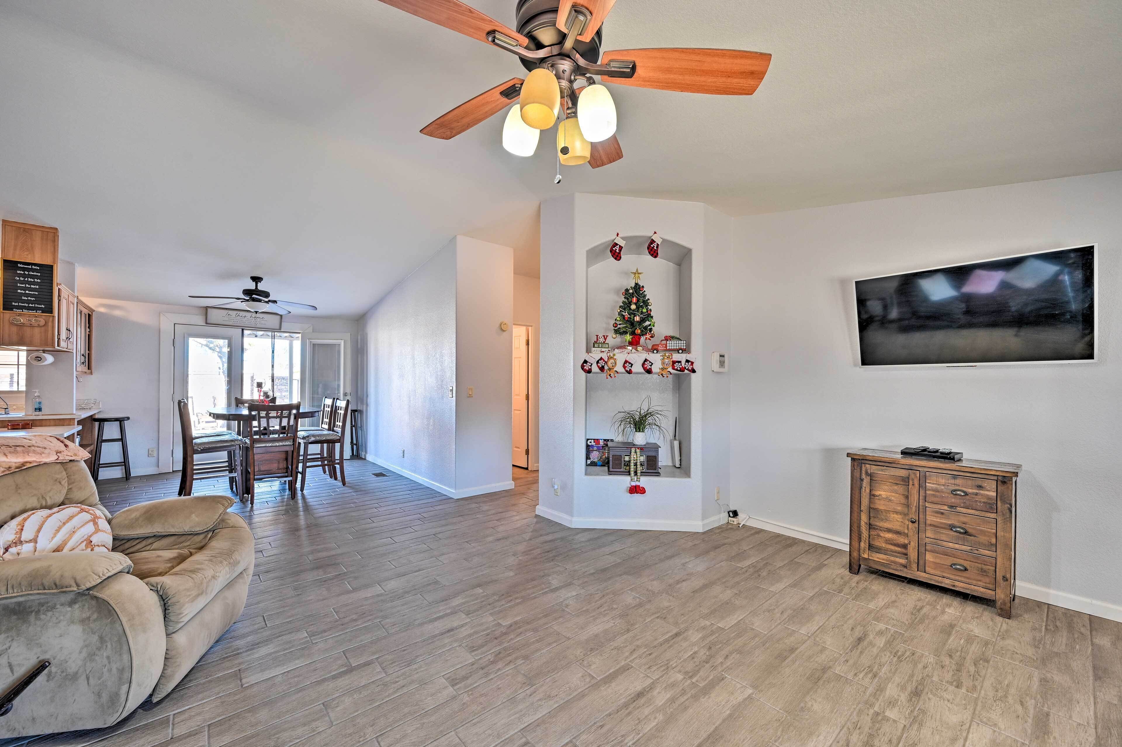 A spacious living room with a ceiling fan, a television mounted on the wall, and a dining area with wooden chairs and a table.