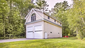 A two-story house with a garage, surrounded by a forested area. - Readfield Retreat w/ Lake Maranacook Views! (Readfield)