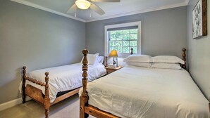 Une chambre à coucher avec deux lits en bois, un ventilateur de plafond, une fenêtre et une table de chevet avec une lampe.