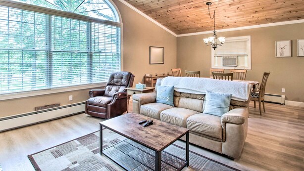 A cozy living room with a large window, a leather armchair, a beige sofa, and a wooden coffee table. - Readfield Retreat w/ Lake Maranacook Views! (Readfield)